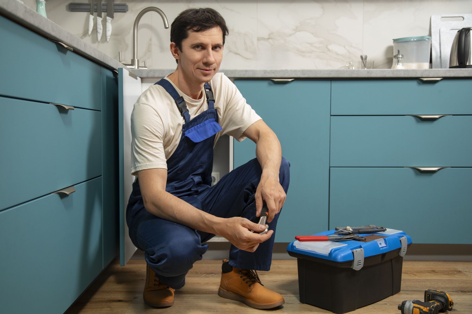 A Copperline plumber kneeling beside an open kitchen cabinet with his toolbox