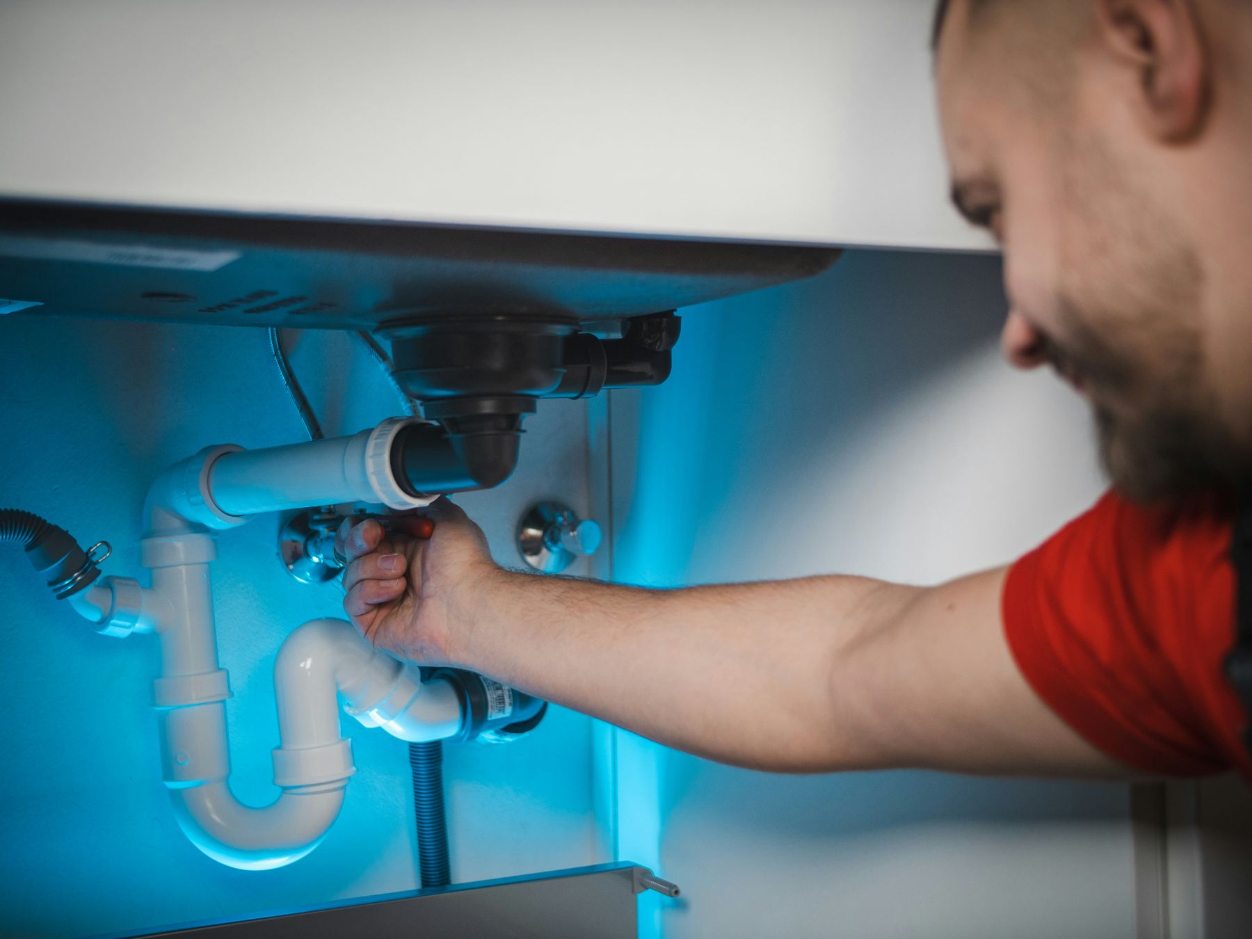 Close-up of a plumber's hand tightening a fitting under a kitchen sink